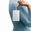 Biały powerbank z okrągłym symbolem błyskawicy na środku jest zawieszony na palcu osoby ubranej w niebieski, prążkowany sweter. Produkt ma prostokątny kształt i zaokrąglone krawędzie.