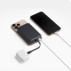 Na zdjęciu znajduje się szary powerbank podłączony do dwóch smartfonów oraz białego etui na słuchawki bezprzewodowe. Powerbank jest umieszczony na jednym z telefonów, a do każdego urządzenia prowadzi osobny kabel.