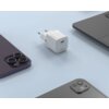 Na zdjęciu znajduje się biała ładowarka sieciowa z napisem "PD 20W" oraz "FIXED" na obudowie, umieszczona na jasnoniebieskim tle obok dwóch smartfonów i fragmentu laptopa.