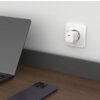 Na zdjęciu znajduje się biały adapter sieciowy wpięty do gniazdka na ścianie, z widocznym napisem "FIXED 20W". Obok na drewnianym blacie leży ciemny smartfon oraz fragment otwartego laptopa.