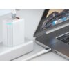 Na zdjęciu widoczny jest biały kabel USB-C podłączony do laptopa oraz do białej ładowarki z niebieskim podświetleniem. Laptop ma otwarty ekran z widocznymi ikonami aplikacji na pasku.