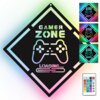 Czarny, diamentowy znak z napisem "GAMER ZONE" i grafiką kontrolera do gier, poniżej napis "LOADING..." z paskiem ładowania. Obok znajdują się trzy mniejsze wersje znaku w różnych kolorach oraz pilot z przyciskami w różnych kolorach i oznaczeniami.