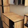Zestaw mebli łazienkowych wiszących w kolorze dąb craft z czarnymi akcentami, składający się z szafek z pięcioma drzwiami, dwudziestoma jedną półką i dwiema szufladami. Na zdjęciu widoczne są drewniane fronty oraz otwarte półki z umieszczonymi na nich prz