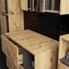 Zestaw mebli łazienkowych wiszących w kolorze dębu Artisan z grafitowymi elementami, posiadający otwarte szuflady i półki, na których widoczne są kosmetyki. Tło stanowi czarna powierzchnia z delikatnym wzorem przypominającym marmur.