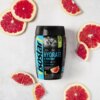 Na zdjęciu znajduje się opakowanie izotoniku "Isostar Hydrate & Perform" o smaku grejpfrutowym, otoczone plasterkami grejpfruta. Na etykiecie widnieje napis: "Hydrate & Perform, Grapefruit Flavour", a także grafika przedstawiająca rowerzystów.