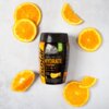 Pojemnik z izotonikiem "Isostar Hydrate & Perform" o smaku pomarańczowym otoczony jest plasterkami pomarańczy na jasnym tle. Na etykiecie widnieje napis: "Hydrate & Perform, Orange Flavour, No Artificial Flavours".