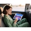 Osoba siedzi w samochodzie, trzymając tablet, na którym widoczny jest tekst: "Supercharge your bedroom living space with a fresh breath from the most impressive light from futuristic energies." oraz obrazek przedstawiający futurystyczne miasto.