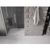 Na zdjęciu widoczna jest kabina prysznicowa z przezroczystymi, rozsuwanymi drzwiami oraz ściana z geometrycznymi płytkami w odcieniach szarości. Obok znajduje się wnęka z półkami, na których stoją różne produkty, a na wieszaku wisi ręcznik.
