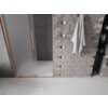 Na zdjęciu widoczne są drzwi prysznicowe z matowego szkła z miedzianą ramą i uchwytem, obok znajduje się ściana z geometrycznymi płytkami oraz zawieszony ręcznik. W tle widać ciemne płytki oraz wnękę z półkami na kosmetyki.