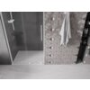 Na zdjęciu znajduje się kabina prysznicowa z przezroczystymi, rozsuwanymi drzwiami oraz białym uchwytem, obok której widać ścianę z geometrycznymi płytkami i zawieszonym ręcznikiem. W tle widoczna jest wnęka z półkami, na których stoją różne produkty.