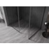 Na zdjęciu znajduje się ścianka prysznicowa typu walk-in z ramką w kolorze gun metal, ustawiona na podłodze z szarych płytek o wzorze marmuru. Ściany prysznica wyłożone są ciemnymi płytkami ułożonymi w jodełkę, a obok znajduje się czarny stolik z butelką.