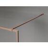 Na zdjęciu widoczna jest ścianka prysznicowa Walk-in z ramką w kolorze miedzi szczotkowanej, zamontowana na szarej ścianie. Produkt ma minimalistyczny design z prostymi liniami i metalowymi elementami.