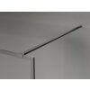 Na zdjęciu widoczna jest ścianka prysznicowa z metalową ramką i wspornikiem, wykonana w kolorze gun gray szczotkowanym. Produkt ma minimalistyczny design i jest zamontowany na gładkiej, szarej ścianie.