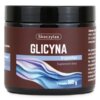 Czarne opakowanie z etykietą w odcieniach brązu i niebieskiego, na której widnieje napis: "Skoczylas GLICYNA tryptofan Suplement diety w proszku 100 g". Etykieta zawiera również kolorową grafikę z falistymi liniami.