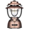 Latarka OLIGHT OL692937 Latarnia biwakowa ma metaliczny, brązowy kolor z przezroczystym kloszem, w którym widoczne są żarówki w stylu retro. Na dolnej części znajduje się logo "OLIGHT" oraz pokrętło do regulacji.