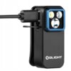 Na zdjęciu znajduje się czarna latarka z niebieską obwódką wokół trzech widocznych diod, podłączona do kabla. Na obudowie widoczne jest logo "OLIGHT".