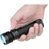 Na zdjęciu widoczna jest czarna latarka trzymana w dłoni, z widocznym napisem "OLIGHT Seeker 4 Pro" na obudowie. Latarka ma niebieską krawędź wokół soczewki i przycisk z symbolem słońca.