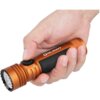 Na zdjęciu widać pomarańczową latarkę trzymaną w dłoni, z widocznym logo "OLIGHT" oraz napisem "Seeker 4 Pro" na czarnej części uchwytu. Latarka ma przycisk z symbolem słońca i żebrowaną głowicę.
