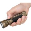 Ręka trzyma latarkę w kolorze brązowym z czarnym uchwytem, na której widoczne są napisy "OLIGHT" oraz "Seeker 4 Pro". Na latarce znajduje się również przycisk z symbolem słońca.