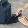 Na zdjęciu widoczny jest grzejnik elektryczny z otwartą osłoną wentylatora, a osoba czyści siatkę ochronną za pomocą szmatki. Tło jest szare i jednolite.