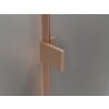 Zdjęcie przedstawia fragment parawanu nawannowego z przezroczystego szkła, z miedzianym, szczotkowanym uchwytem i ramą. Powierzchnia metalu ma delikatną teksturę, a tło jest jednolite i szare.