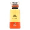 Butelka perfum o gradientowym kolorze, przechodzącym z żółtego do pomarańczowego, z napisem "CORAL BLUSH EAU DE PARFUM" oraz logo "MAISON ALHAMBRA" z wizerunkiem jelenia. Korek butelki jest srebrny z pomarańczowym akcentem.