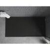 Czarny, prostokątny brodzik prysznicowy o wymiarach 140 x 70 cm, umieszczony na tle ścian wyłożonych szarymi, małymi płytkami mozaikowymi. Na ścianie widoczny jest uchwyt z zawieszonymi białymi ręcznikami.