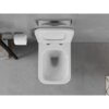 Na zdjęciu widoczna jest biała, połyskująca miska WC typu rimless z deską wolnoopadającą slim, zamontowana na tle szarej, kafelkowej ściany. Obok znajduje się uchwyt z rolką papieru toaletowego oraz fragment drewnianej półki z ręcznikami.