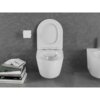 Na zdjęciu znajduje się biała, połyskująca miska WC typu rimless z deską wolnoopadającą slim, zamontowana na tle ciemnej, teksturowanej ściany. Obok miski znajduje się uchwyt z rolką papieru toaletowego oraz stos książek, z widocznymi tytułami na grzbietach.