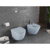 Na zdjęciu znajduje się szara-niebieska matowa miska WC typu Rimless z deską wolnoopadającą oraz bidet, zamontowane na tle ciemnej, teksturowanej ściany. Obok miski WC widoczny jest uchwyt z papierem toaletowym, a na podłodze leżą czasopisma.