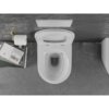 Na zdjęciu widoczna jest biała miska WC z deską wolnoopadającą, umieszczona na tle szarej ściany. Obok znajduje się uchwyt z rolką papieru toaletowego oraz stos książek, z których jedna ma widoczny tytuł "John Ruskin Von Venedig".