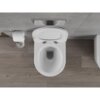 Biała miska WC typu rimless z deską wolnoopadającą slim, wykonana z duroplastu, zamontowana na tle szarej ściany i drewnianej podłogi. Obok znajduje się uchwyt z rolką papieru toaletowego oraz przycisk spłukujący w ścianie.