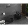 Na zdjęciu znajduje się czarna matowa miska WC typu Rimless oraz bidet zamontowane na ścianie z szarego kamienia. Obok widać uchwyt z papierem toaletowym, stos książek oraz roślinę w doniczce.