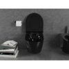 Czarna, błyszcząca miska WC typu Rimless z deską wolnoopadającą slim, zamontowana na tle szarej, teksturowanej ściany. Obok znajduje się uchwyt z rolką papieru toaletowego oraz stos książek z widocznymi tytułami, takimi jak "ART" i "TEXTILES".