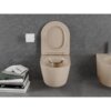 Na zdjęciu znajduje się miska WC w kolorze cappuccino mat z deską wolnoopadającą, zamontowana na tle ciemnoszarej ściany. Obok miski znajduje się uchwyt z rolką papieru toaletowego oraz stos książek, na których widoczne są tytuły takie jak "Volker Hinz", "ART", "NEW ULTIMATE HOUSING", "TEXTILES", "BOCCA" i "VIRGIL ABLOH".