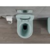Na zdjęciu widoczna jest jasna, matowa, zielona miska WC typu rimless z deską wolnoopadającą slim, zamontowana na tle szarej ściany z drewnianą podłogą. Obok znajduje się uchwyt z rolką papieru toaletowego oraz przycisk spłukujący na ścianie.