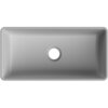 Prostokątna, szara jasna matowa umywalka nablatowa z centralnie umieszczonym otworem odpływowym. Produkt ma gładką powierzchnię i zaokrąglone rogi.