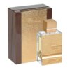 Złoty flakon perfum z napisem "Haramain Amber Oud" oraz "Gold 999.9 Dubai Edition" stoi obok brązowego pudełka z tekstem "Al Haramain Since 1970". Oba elementy mają teksturowaną powierzchnię, która odbija światło.