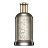 Przezroczysta butelka perfum z metalicznym korkiem, na której widnieje wytłoczony napis "BOSS" oraz mniejszy napis "HUGO BOSS" w kolorze złotym. Butelka ma elegancki, minimalistyczny design.