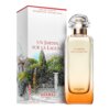 Na zdjęciu znajduje się flakon perfum oraz pudełko z napisem "UN JARDIN SUR LA LAGUNE" i "HERMES PARIS". Pudełko ozdobione jest rysunkiem ogrodu z drzewami i murem, a na flakonie widnieje ten sam napis co na pudełku.