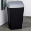 Czarny plastikowy kosz na śmieci o pojemności 38 litrów z szarym, zaokrąglonym wiekiem, stoi na betonowej podłodze obok ściany z zawieszonym zielonym ręcznikiem. Kosz ma pionowe żłobienia na powierzchni.
