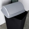 Czarny plastikowy kosz na śmieci o pojemności 38 litrów z szarym, zaokrąglonym wiekiem. Kosz stoi na podłodze przy jasnej ścianie.
