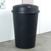 Czarny, plastikowy kosz na śmieci o pojemności 47 litrów stoi na podłodze, obok białej szafki. Kosz ma zaokrągloną pokrywę z małym, okrągłym przyciskiem na górze.
