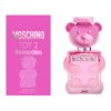 Różowe opakowanie i flakon w kształcie misia z napisem "MOSCHINO TOY 2 BUBBLE GUM" oraz "EAU DE TOILETTE 100 ML / 3.4 US FL. OZ." na opakowaniu. Flakon również ma napis "MOSCHINO" na przodzie.
