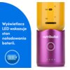 Fioletowy blender personalny z logo "nutribullet" i przyciskiem zasilania, na którym znajduje się żółty pojemnik z miarką w mililitrach i uncjach. Obok widnieje niebieski panel z tekstem: "Wyświetlacz LED wskazuje stan naładowania baterii" oraz ikoną baterii.