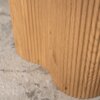Fragment okrągłego stolika kawowego z widoczną fakturą drewna w kolorze dębu, stojącego na jasnym, wzorzystym dywanie.