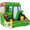 Zabawka w kształcie zielonego traktora z dużymi oczami, umieszczona w opakowaniu z napisem "Johnny Push N Roll" oraz logo "John Deere". Na opakowaniu widnieje również napis "18m+" i logo "TOMY".
