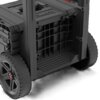 Czarna mobilna skrzynia z dużymi kołami, posiada kratkowaną strukturę na boku oraz widoczne logo "QBRICK System". Na górnej części skrzyni znajdują się uchwyty i wytłoczone napisy.
