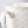 Biały ceramiczny kubek o pojemności 580 ml z wytłoczonym wzorem serc na powierzchni. Uchwyt kubka jest gładki i błyszczący.