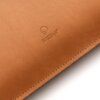 Jasnobrązowe etui na laptopa z widocznym logo "BALTAN" wytłoczonym na powierzchni. Produkt wykonany jest z gładkiego materiału, z widocznymi przeszyciami wzdłuż krawędzi.